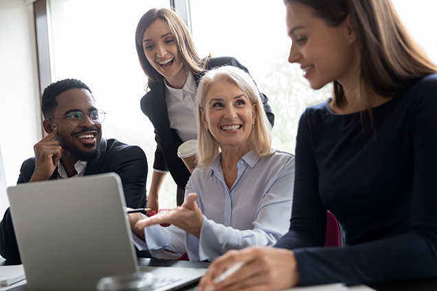 Elder female mentor teaching interns to create project on laptop